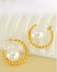 Macro shot of gold-plated C-shaped textured earrings with large white pearls and ear studs