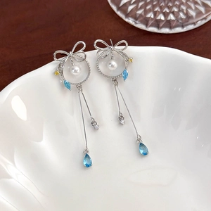 Macro shot of silver bow tassel earrings with white pearls and colorful crystals