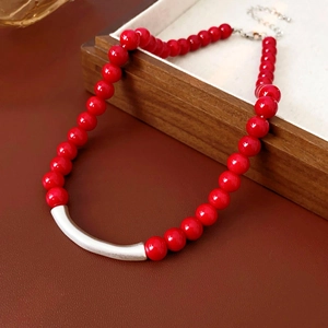 Détail du collier de perles rouges avec barre en argent sur plateau en bois