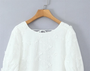 Detail van een witte jurk met 3D-bloemborduursels en een striksluiting in de nek