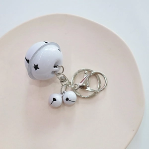 Close-up of white metal bell keychain with star cutout and silver lobster clasp on tray