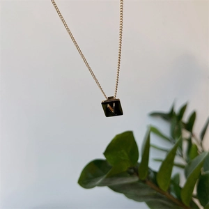 Macro shot of gold square pendant necklace with black enamel and letter V on fine chain
