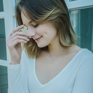 Close-up of a silver cross necklace and moissanite ring worn by a model in soft light
