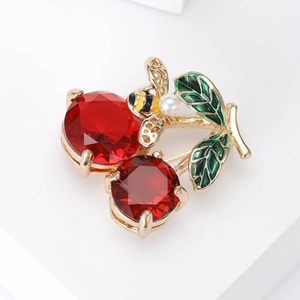 Close-up of cherry brooch with red faceted gems, green enamel leaf, and gold bee detail