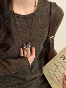 Close-up of a vintage horse pendant necklace on a brown sweater with retro vibes
