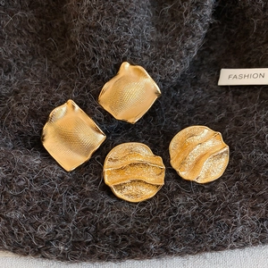 Détail macro des boucles d'oreilles froissées plaquées or et clous carrés texturés