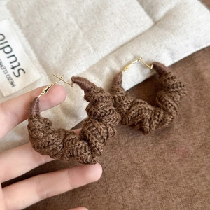 Gros plan sur des boucles d'oreilles en laine marron avec texture crochetée à la main
