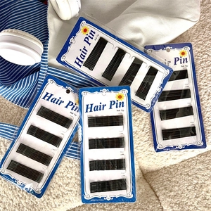 Close-up of black wave-shaped bobby pins with ball tips on white textured background