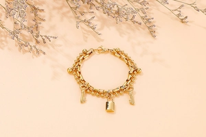 Macro detail of golden double-layer bead and box chain bracelet with lock and key charms