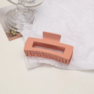 Macro detail of a large matte salmon pink hair claw clip on white textured paper