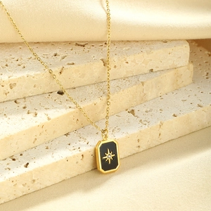 Macro view of gold chain with black enamel starburst pendant on stone background