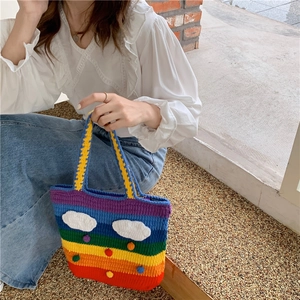 Close-up of rainbow knit bag with white cloud patches held by a model in casual attire