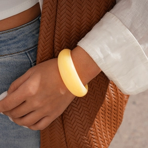 Detailed view of wide cream resin cuff bracelet on model with urban casual attire
