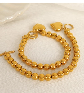 Detail of two gold beaded bracelets with heart pendants and toggle clasps on fabric