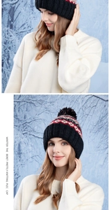 Detail of winter knitted beanie with ethnic patterns and black faux fur pompom in snow