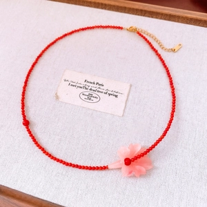 Detailed macro view of red beaded necklace with pink flower pendant and gold clasp