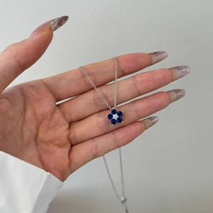 Detail of flower pendant necklace with blue gemstones held by hand in clear macro view