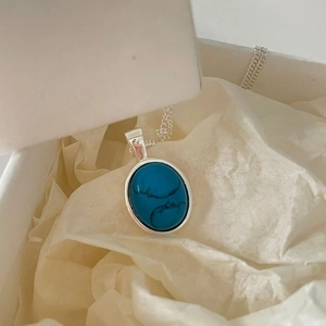 Macro shot of a 925 sterling silver necklace with an oval turquoise pendant on white tissue