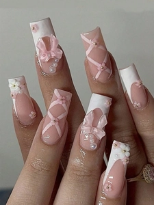 Close-up of French tip press-on nails with 3D pink bows, white flowers and pearls