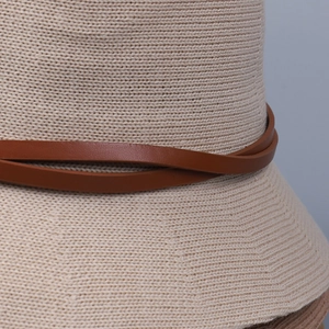 Close-up of beige knitted sun hat showing wavy texture and brown leather strap detail