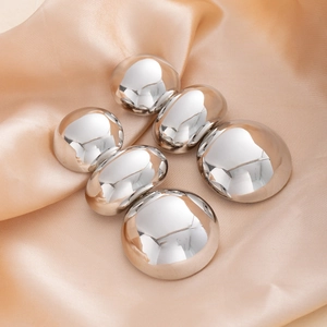 Detailed view of polished silver geometric earrings on elegant champagne silk fabric