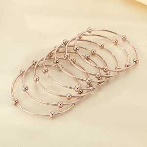 Detailed view of seven stacked rose gold bracelets with beads on textured silk background