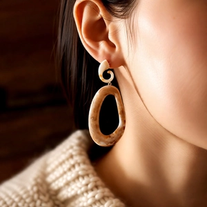 Close-up of tortoise shell acrylic oval drop earrings worn with a beige knit sweater
