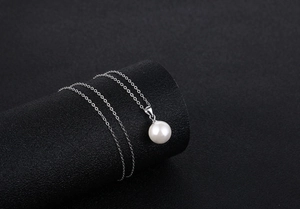 Close-up of a glossy white pearl pendant on a thin silver chain over a black background
