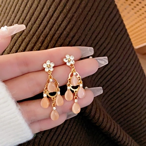 Close-up of gold dangle earrings with pink teardrop stones and rhinestone flower detail