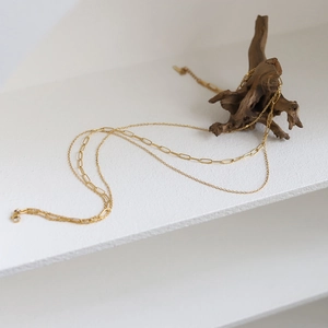Gold layered necklace with paperclip and round link chains on natural wood and white steps
