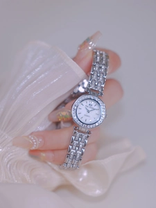 Close-up of silver luxury women's watch with rhinestones worn on wrist with white fabric