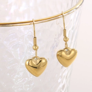 Détail de boucles d'oreilles cœur dorées en acier inoxydable sur un bord de verre avec bokeh