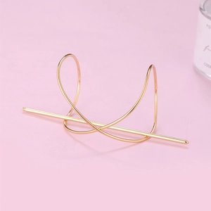 Minimalist gold metal hair pin with cross-wrapped geometric base on pink background