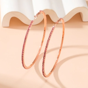Close-up of 8cm rose gold hoop earrings with pink rhinestones on a warm beige background