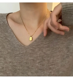Detailed close-up of a golden square pendant necklace on a bead chain worn by a female model
