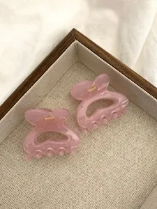 Détail de pinces à cheveux en acrylique rose avec ressorts dorés sur un plateau tressé