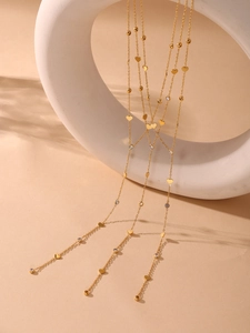 Détail du collier en Y doré avec breloques cœur et zircons sur support géométrique blanc