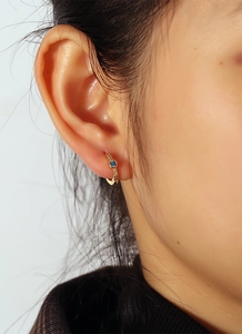 Detail of gold hoop earrings with white zircons and a blue gemstone on a model