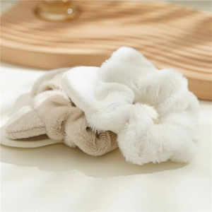 Detail of plush faux fur hair scrunchies in white and beige on a soft textured surface