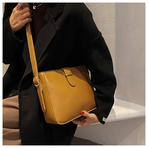 Detail of yellow leather bucket bag worn with a black coat for a stylish contrast look