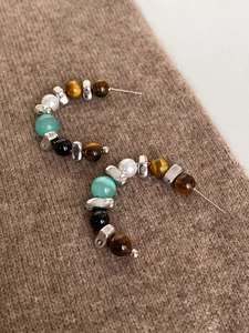 Detail of C-shaped beaded earrings featuring tiger eye stones and pearls on brown knit