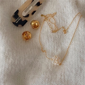 Detail of a gold floral pearl necklace and sphere earrings on a soft white knit surface