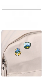 Detail of outdoor camping enamel pins showing a coffee cup and wilderness tent on a canvas bag