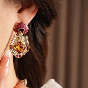 Close-up of vintage gold earrings with amber stone and pink enamel worn by a model