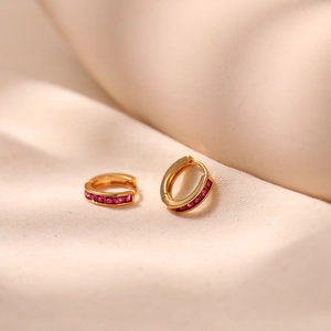 Close-up of gold hoop earrings with red zircon stones on a soft beige fabric