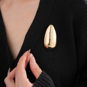 Detail of a shiny gold irregular oval brooch styled on a black cardigan sweater