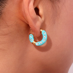 Close-up of sky blue enamel and gold-plated C-shaped hoop earrings with white zircons