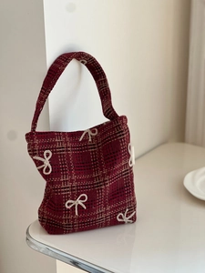 Detail of red and black plaid fabric handbag with 3D white bows in a minimal setting