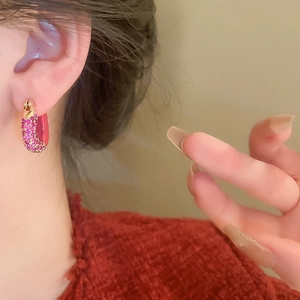 Close-up of a U-shaped gold earring with pink zircon inlay worn by a model in red sweater