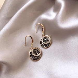 Elegant gold drop earrings with circular black and white crystals on silk background